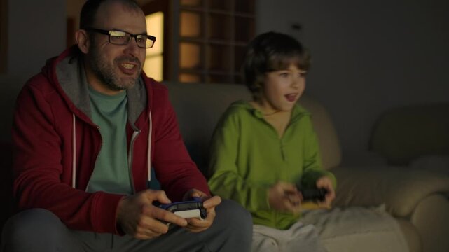 Father and Son Expressing Emotions While Enjoying Relaxing Together, Playing Video Games in Front of TV.  Family Time Hobby. Family Having Fun Together at Home in Living Room Playing Video Games.