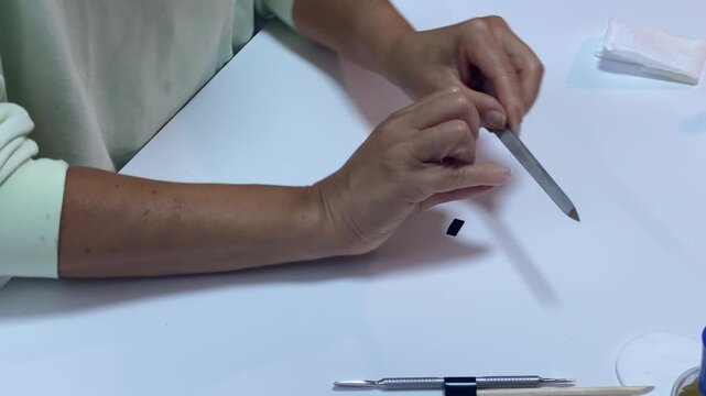 A focused person rapidly files their fingernails with a metal file. The hands move smoothly over a clean white desk, creating a peaceful and satisfying feeling.