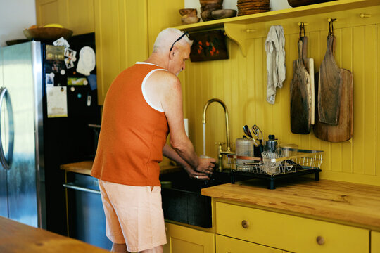man washing dishes at his kitchen sink at home