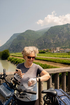 Senior woman cyclist checking smartwatch by Adige River in Italy