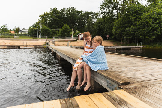 Mother and daughter wrapped in towels dangling feet in lake