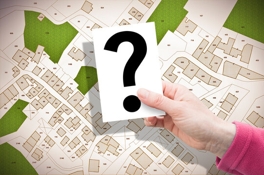 Imaginary cadastral map of territory with buildings and land parcel - concept with hand holding a card with question mark