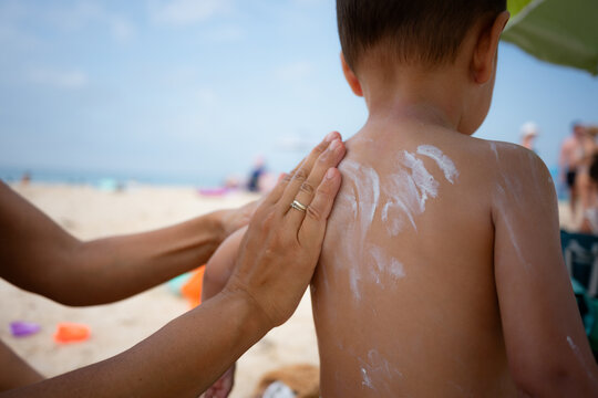 Parent applying sunscreen on child's back at beach