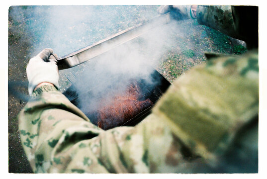 Unrecognized man grilling fish over a smoky charcoal barbecue outdoors