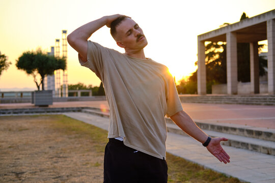 medium shot of Man stretching neck in park at sunset