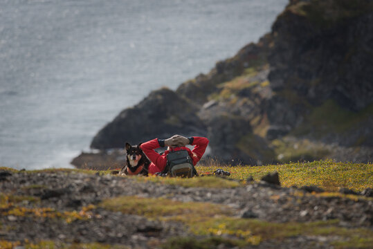 Woman in red jacket and dog resting overlooking a rocky shore
