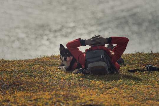 Hiker in red jacket and dog resting in the sun with ocean below
