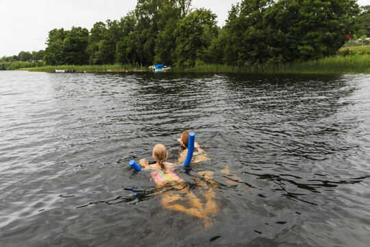 Mother and daughter swimming in lake with pool noodle