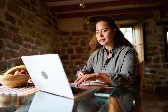 Woman working online from rustic home with laptop