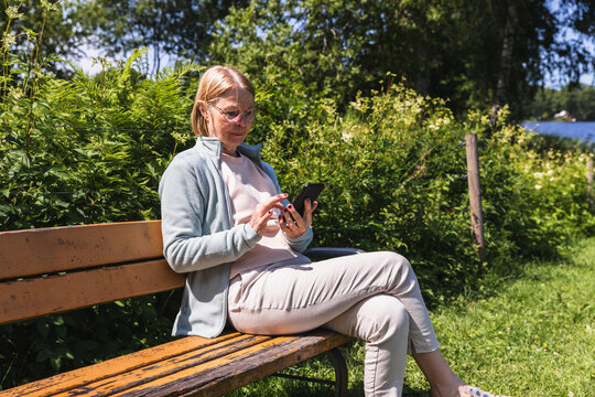 Senior woman sitting on park bench using smartphone