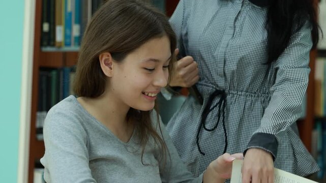Caucasian teenage girl smiles softly in library. She wears light green headphones and a gray sweater. Background shows blurred rows of book shelves. Education, Back to school
