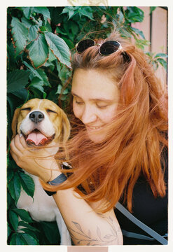 A woman cuddles her beagle among lush green vines