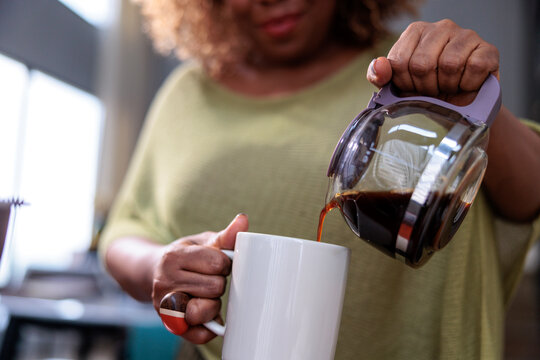 A woman pours fresh coffee into a white mug