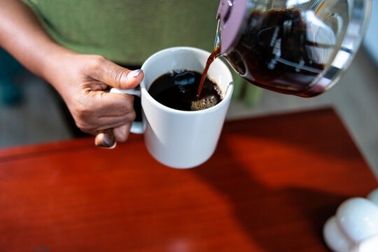 Pouring fresh black coffee into a white mug