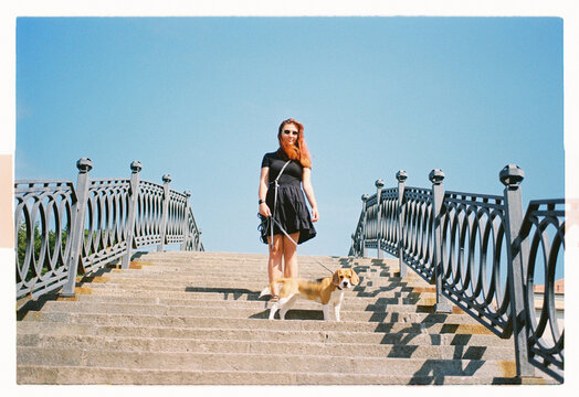 A red-haired woman and her beagle pause on grand stone steps