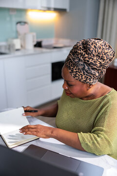 Woman in a leopard headwrap writing in a notebook.