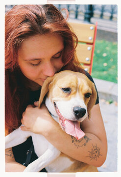 A woman nuzzles her beagle puppy on a park bench