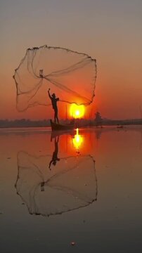 Silhouette of fisherman throwing fishing net into lake during golden sunset
