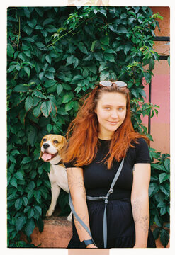 A red-haired woman and her beagle against an ivy wall