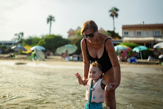 Grandmother teaching grandchild to walk in ocean water