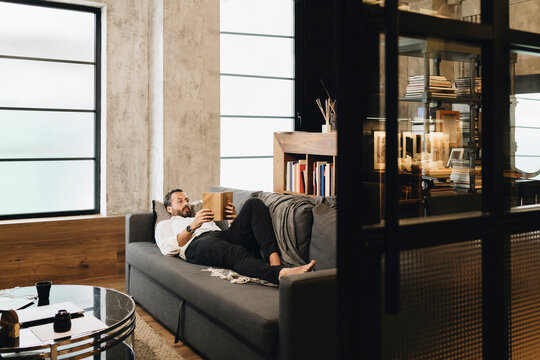 Person relaxing on sofa reading book at home