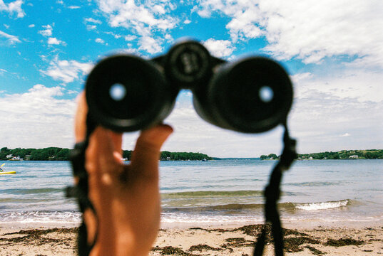 POV view of hand holding binoculars at the beach on film