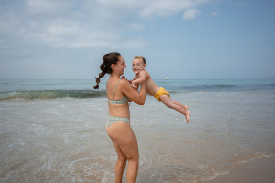 Mother lifting toddler playing in ocean water
