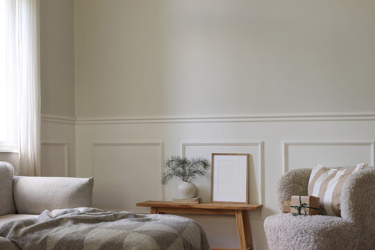 Elegant Christmas Scandinavian interior. Vertical wooden picture frame mockup, poster. Wooden table. Vase pine tree branches. Wrapped gifts, wool armchair. Sofa in living room near window, winter home
