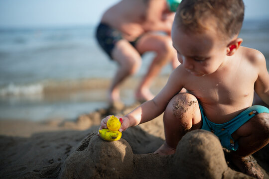 Toddler playing with toy duck on sandcastle at beach
