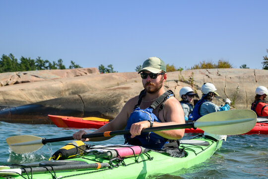 Sea kayaker in a green kayak in front of a group of helmeted paddlers beside granite islands on Georgian Bay, Ontario, Canada