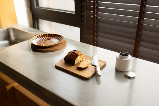 Sliced Loaf Cake on Wooden Board by Kitchen Sink and Window Blinds