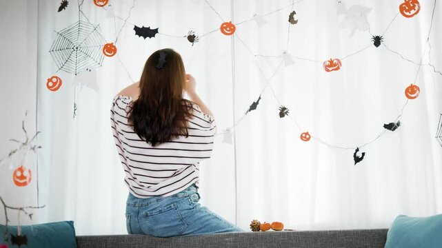 woman decorating her domestic space for a spooky Halloween party celebration.Keeping up the festive autumn traditions, she carefully hangs the paper ornaments on bright windows.High quality 4k footage