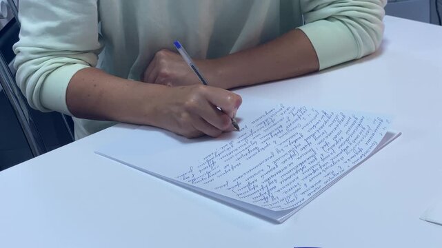 A student writes notes carefully on white paper with a pen. She sits calmly at a bright white desk. Her quiet focus creates a serene and peaceful atmosphere.
