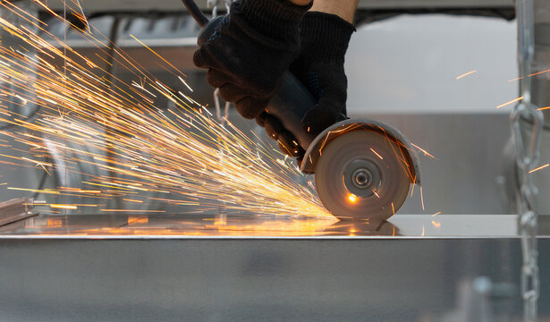 a worker in protective gloves cutting a metal with an angle grinder