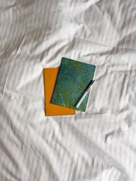 Overhead Flat Lay of Colorful Notebooks and Pen on White Bedding