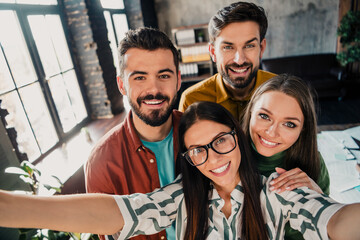 Fototapeta premium Young creative team of coworkers and friends taking a happy group selfie together in a modern loft office workspace, smiling and celebrating collaboration and team spirit