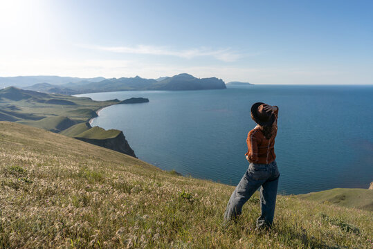 Woman hat hills, young woman in a hat standing on grassy hill overlooking a vast blue bay during a sunny day