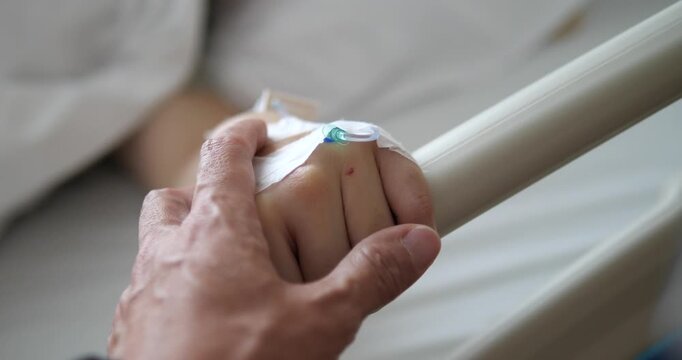 Close up of holding patient hand with IV saline solution in hospital