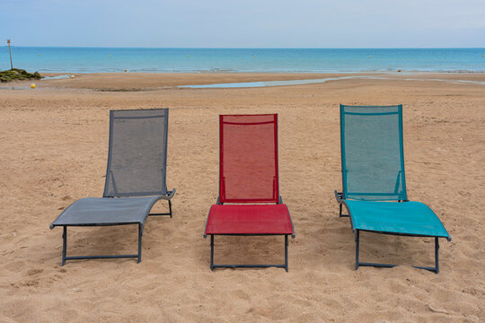 Langrune-Sur-Mer, France - 08 09 2026: Three beach chairs blue, red, and gray on the beach with the sea in the background.