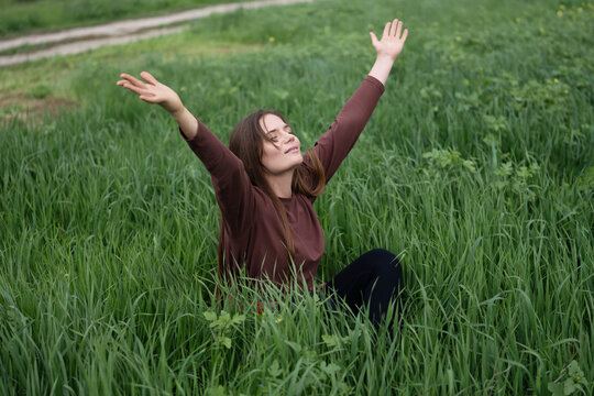Freedom expression featuring a young woman sitting with raised arms in a lush green meadow during the daytime