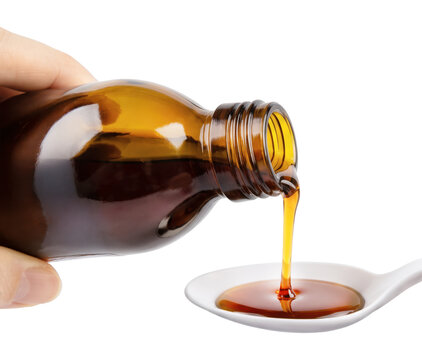 Amber medicinal syrup is being poured from a glass bottle in a white spoon isolated on white