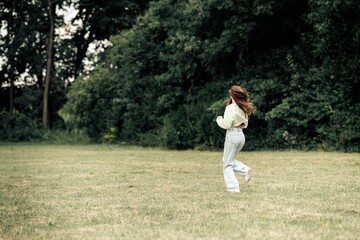 Obraz premium Young woman running across a grassy park field in casual outfit enjoying nature and freedom on a breezy day