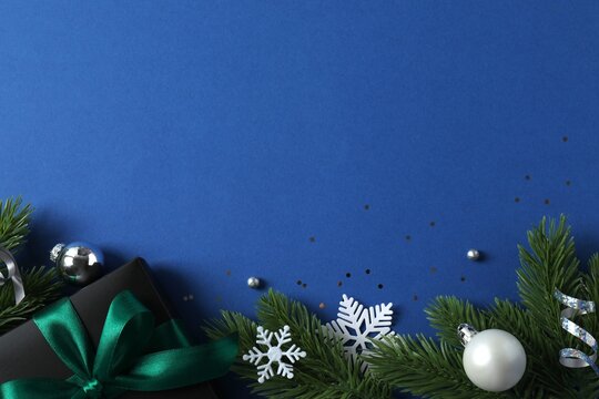 Top view of gift box with green bow and Christmas decorations on blue background, space for text