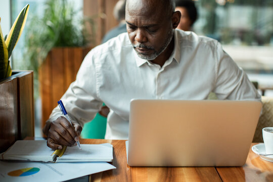 Man writing notes while working on laptop in cafe