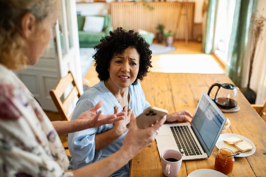 Woman reacts as companion shows phone while working on laptop at home