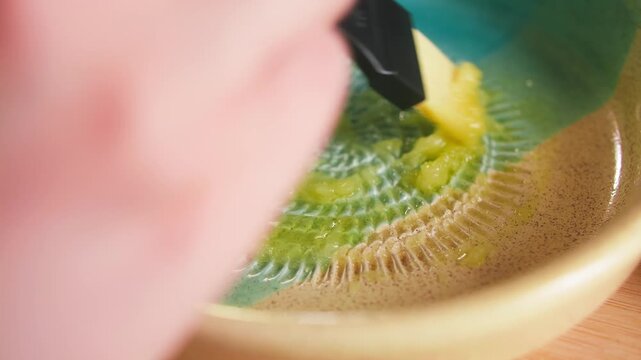 Close-up of fresh garlic being grated into a smooth paste on a traditional Spanish ceramic grater plate. Authentic Mediterranean cooking and food preparation.