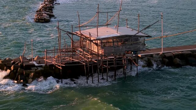 San Vito Chietino Costa dei Trabocchi Abruzzo Italy drone 70mm telephoto golden sunrise close up. Aerial view of wooden trabocco fishing platform on pier, waves crashing, natural audio 4K. 