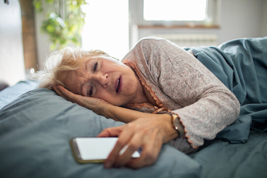 Elderly woman in bed reaching for smartphone in distress