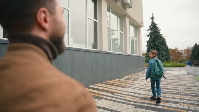 Family in city near school building. Man father and little girl daughter walking to studying at morning dad touching nose of baby say goodbye to child kid going to learning primary elementary class
