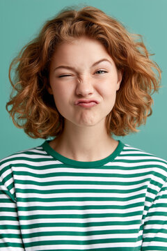 Young woman making a funny pouty face and winking against green background.